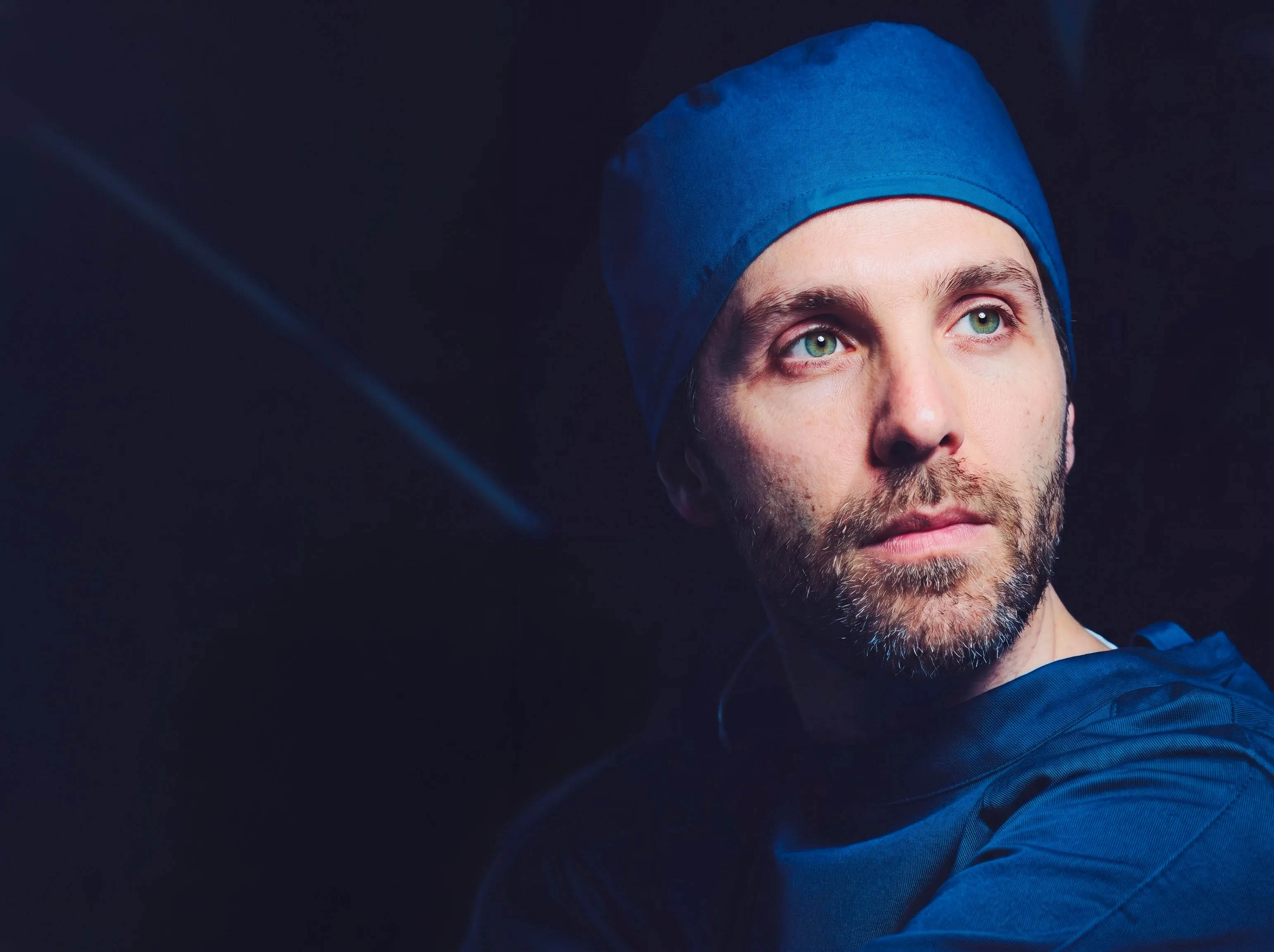 Dr. med. René Raboch in Op-Haube, seitlich angeleuchtet vor dunklem Hintergrund